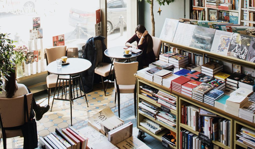 Person sitting at a table in a bookstore reading a book.