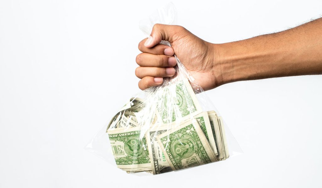 A hand holding a plastic bag of money