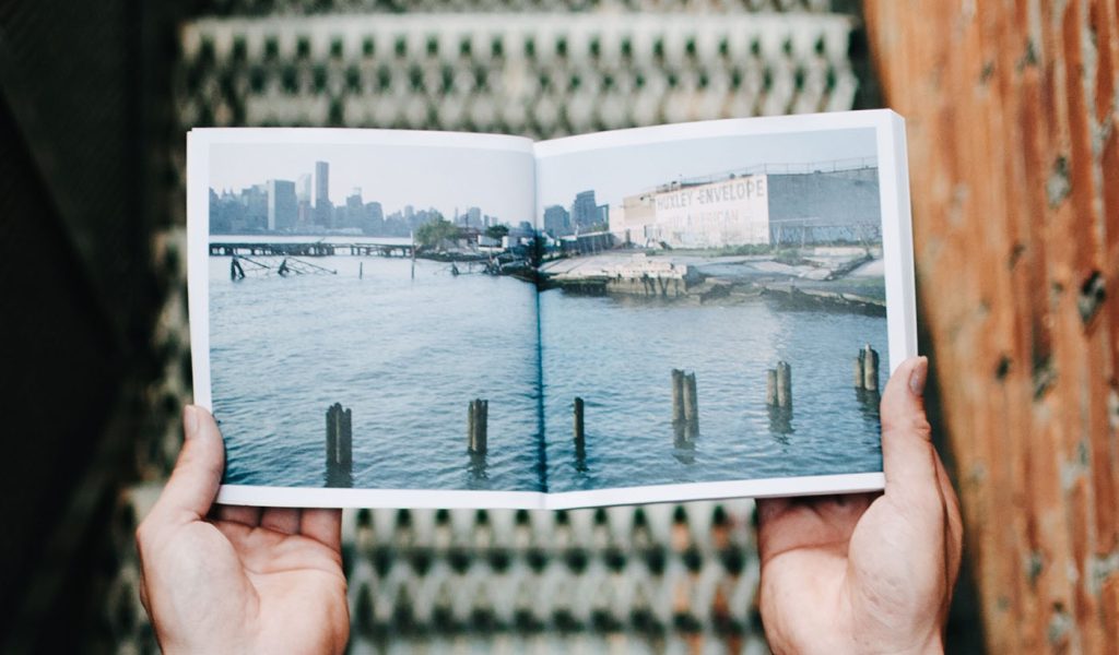 Person holding a photo book open with a picture of a peaceful water scene.