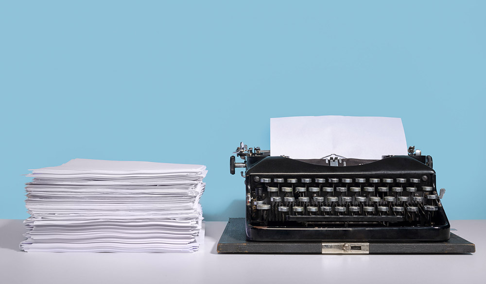 Stack of white papers next to a black typewriter with a blue background