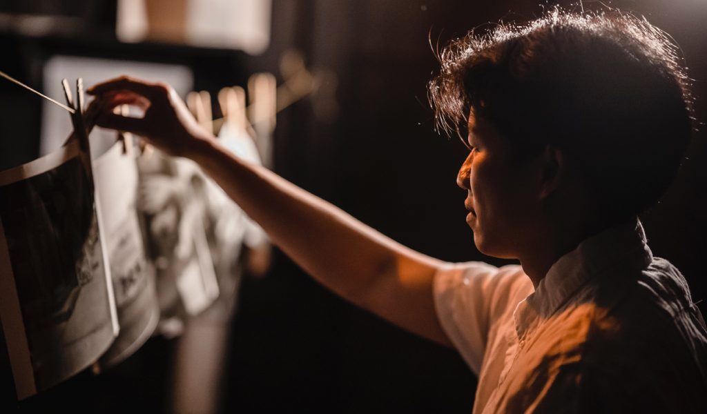 Photographer hanging print photos in a dark room.