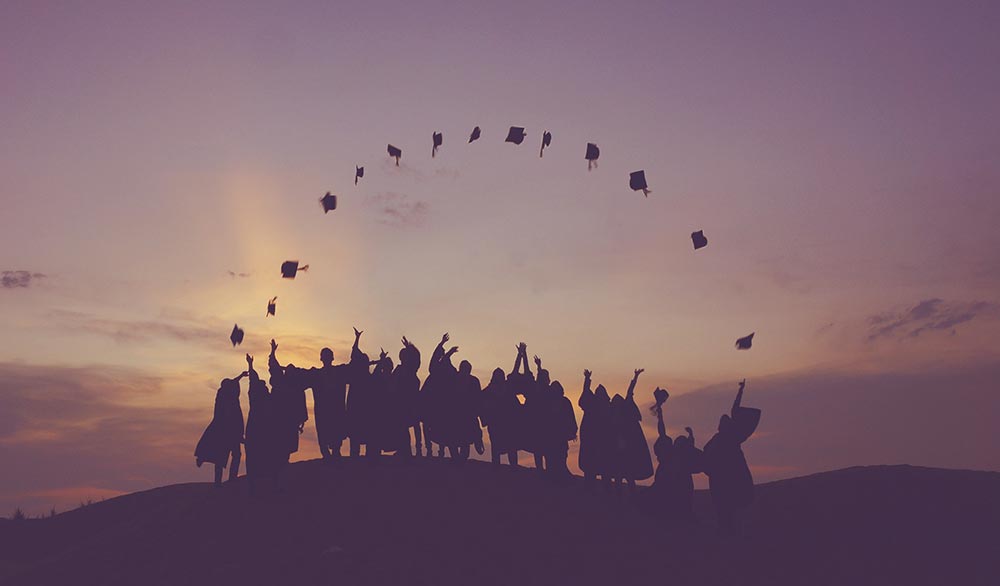graduates in gowns throwing their caps in the air in front of the sunset