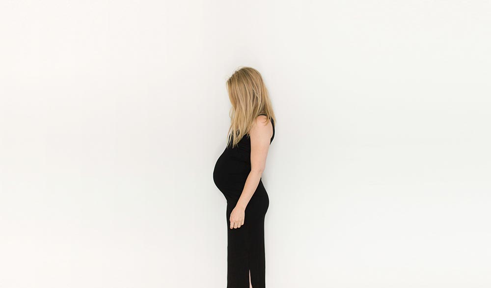 Pregnant woman in a black dress against a white background