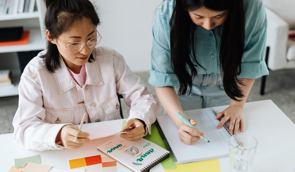 Two graphic design students working on their portfolios, one with a notebook and one with color swatches.