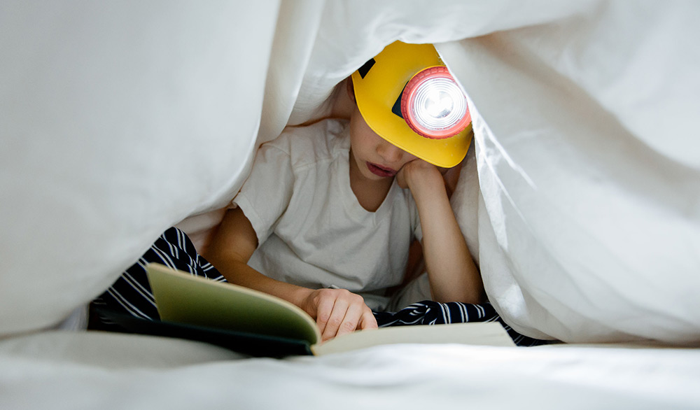 kid reading under covers