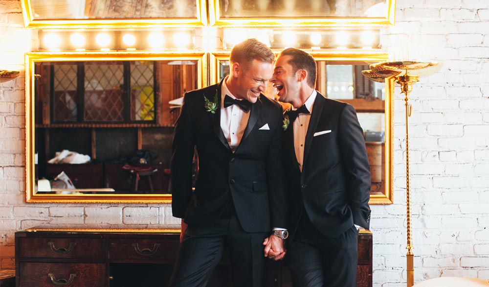Two grooms holding hands and laughing