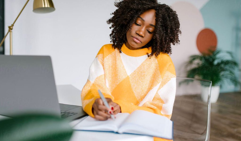 Person writing in a custom planner in an orange sweater.