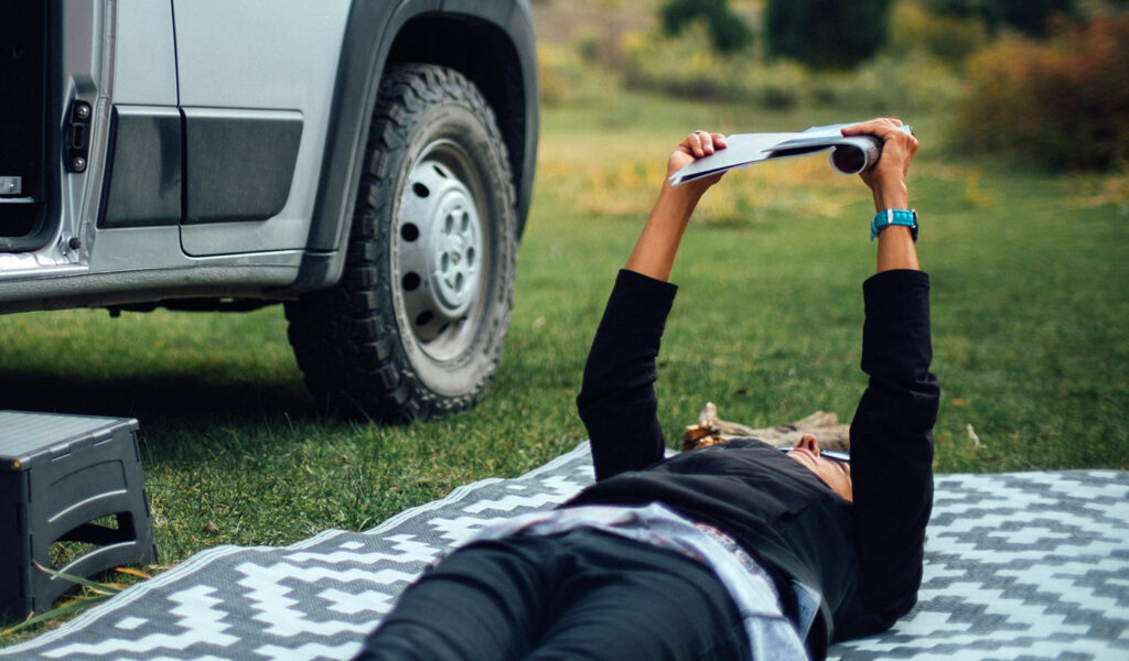 Person laying on blanket in grass reading.