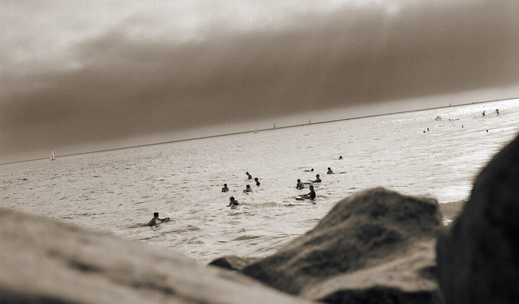 Black & White ocean scene of surfers in the water viewed from behind rocks.