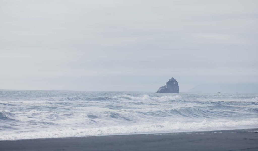 Waves at shore line with large rock on horizon