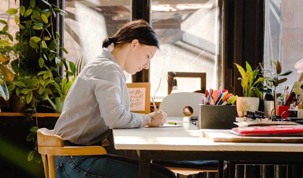 Person sitting at a desk writing a book design software pros & cons list