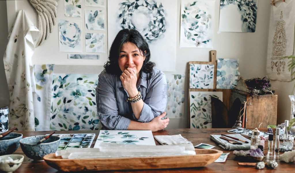 Stephanie Ryan, artist, sitting at her desk surrounded by her finished watercolor art