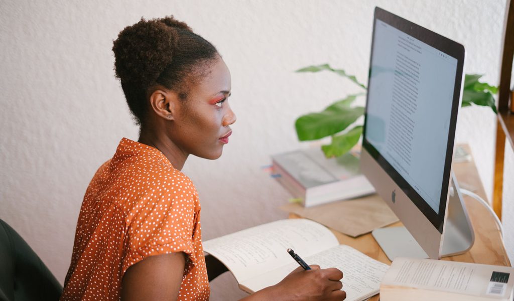 Person sitting in front of a computer screen reading about self-publishing and taking notes