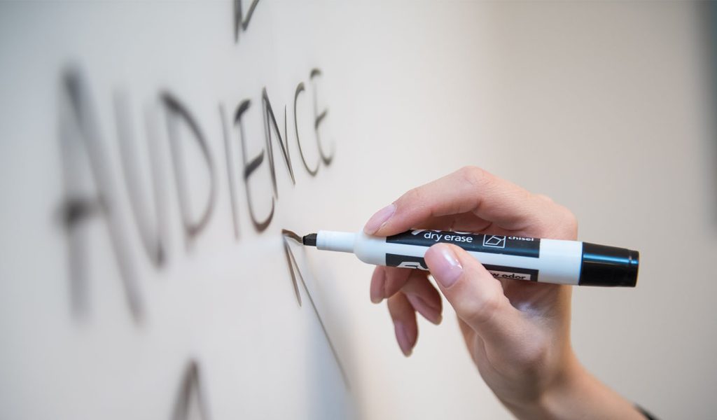 Person writing the word "audience" on a white board