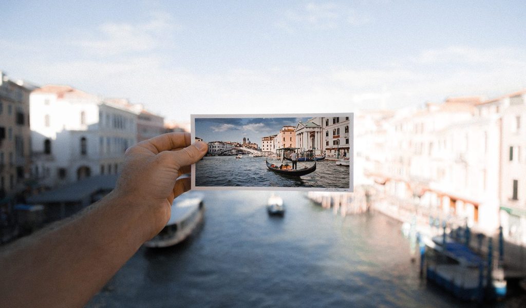 Person holding a photo of the Venice canals in front of the same scene