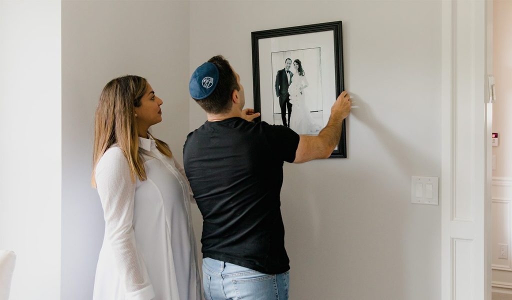 Two people hanging a picture of themselves getting married on their wall