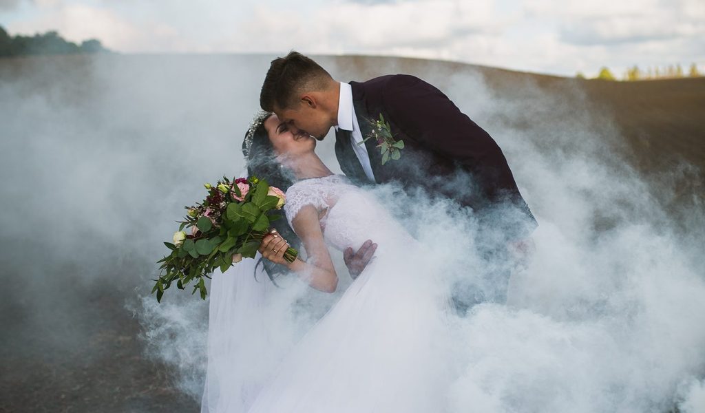 Bride and groom kissing surrounded by a cloud of smoke