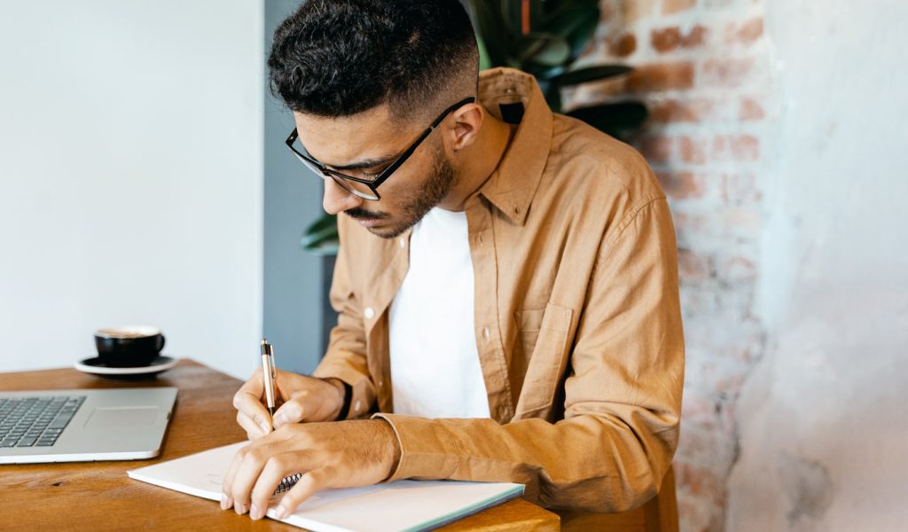 Person writing in a notebook, planning their writing portfolio.