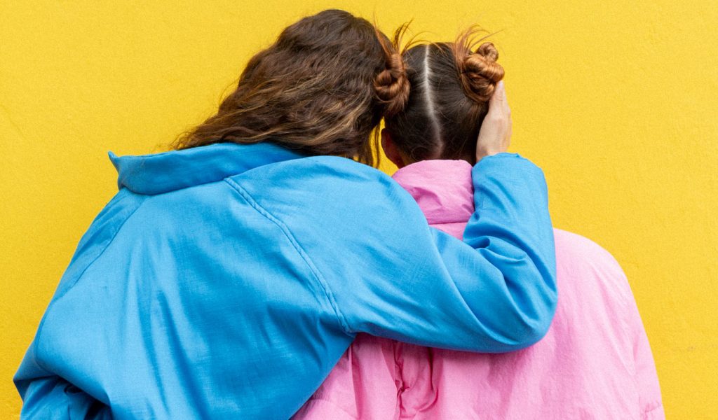 Two people's backs in bright sweatshirts and yellow background
