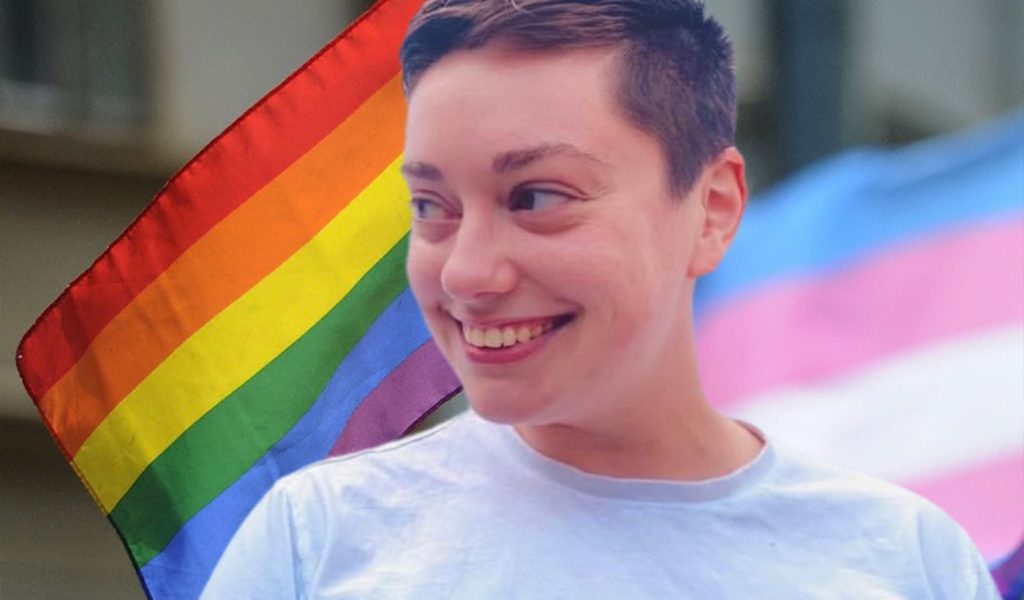 Sarah Kate Smigiel smiling with pride and trans flags behind them
