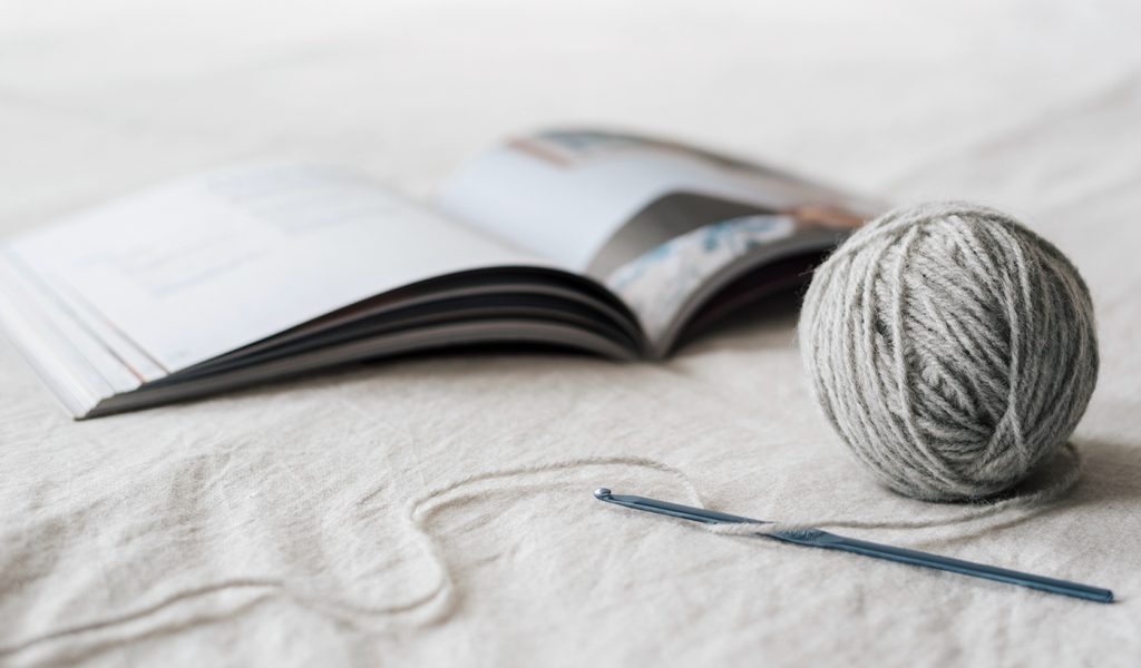 Ball of grey yarn and a zine about knitting open on a bed.