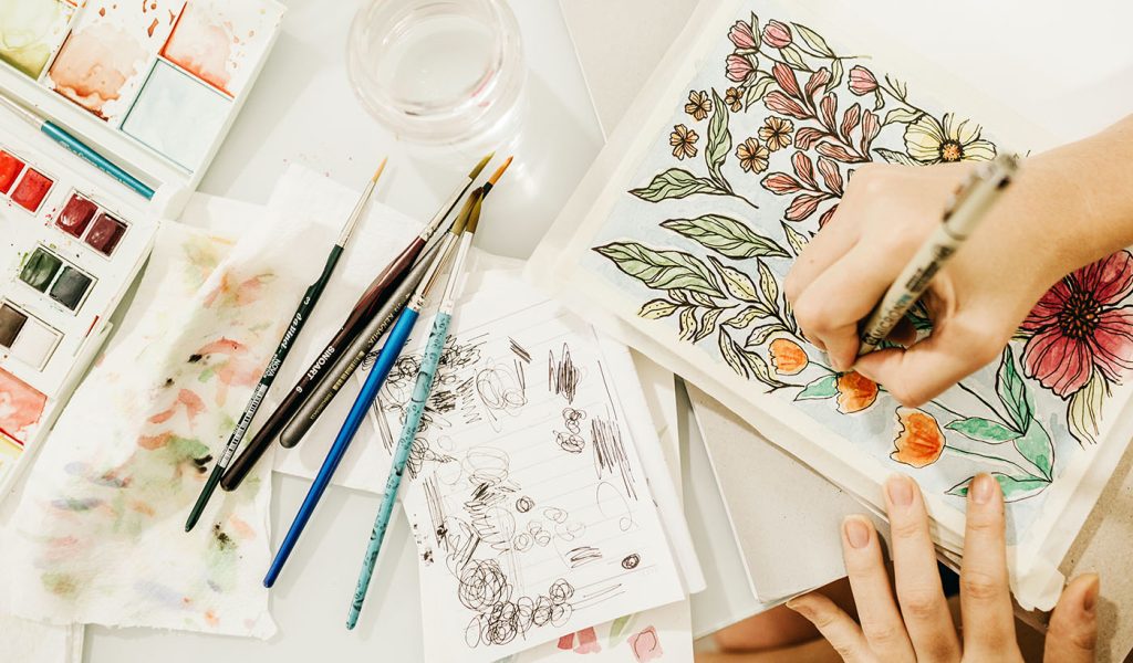 Artist sketching and watercoloring a children's book of flowers.