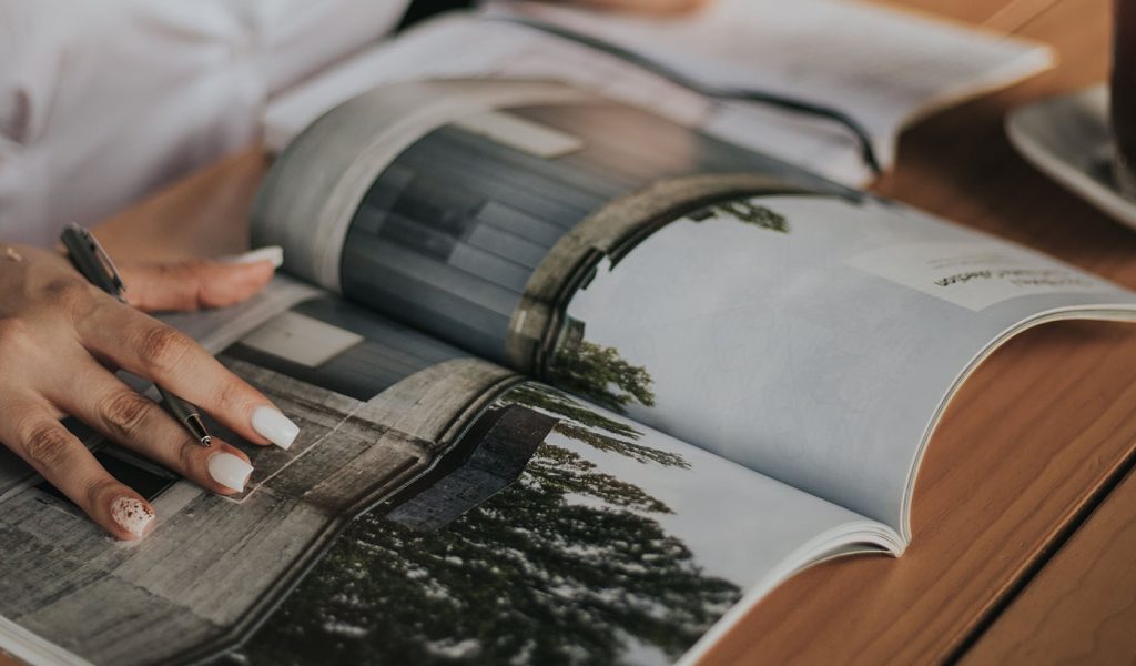 Person holding a magazine with a pen in their hand