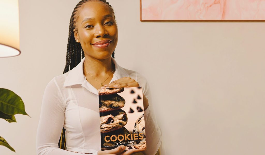 Secoyah Browne holding self published cookbook Cookies by Chef Coy