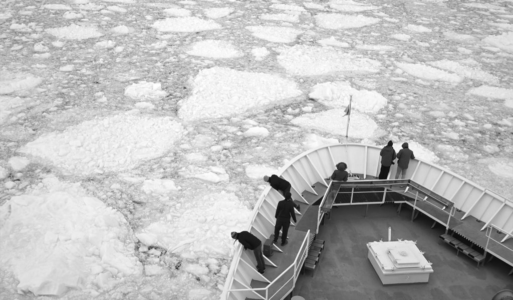 black and white photo of a ship on an Antarctic expedition with explorers taking in the surroundings by Dan Milnor