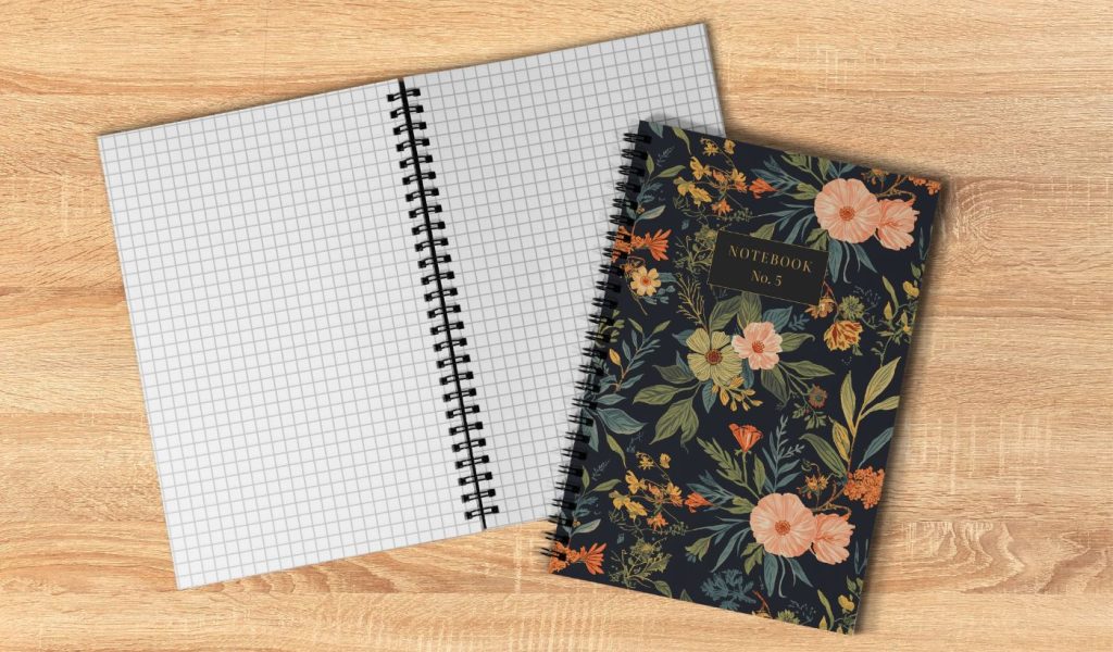 A Wire-O notebook with a floral cover design and lined grid interior pages, shown open and closed on a wooden surface. 